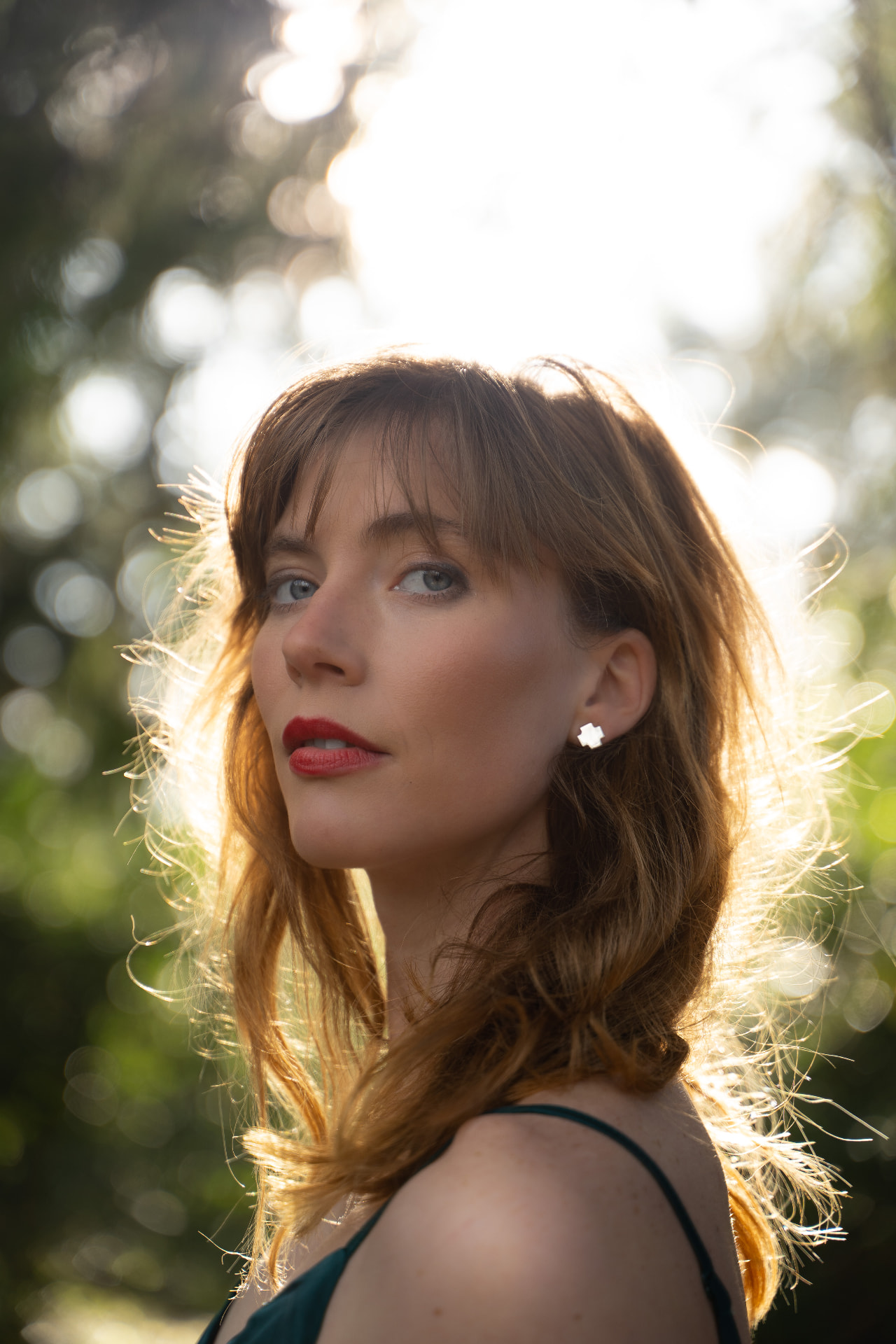 Golden-hour portrait of a woman with red lipstick and windswept hair backlit by the sun