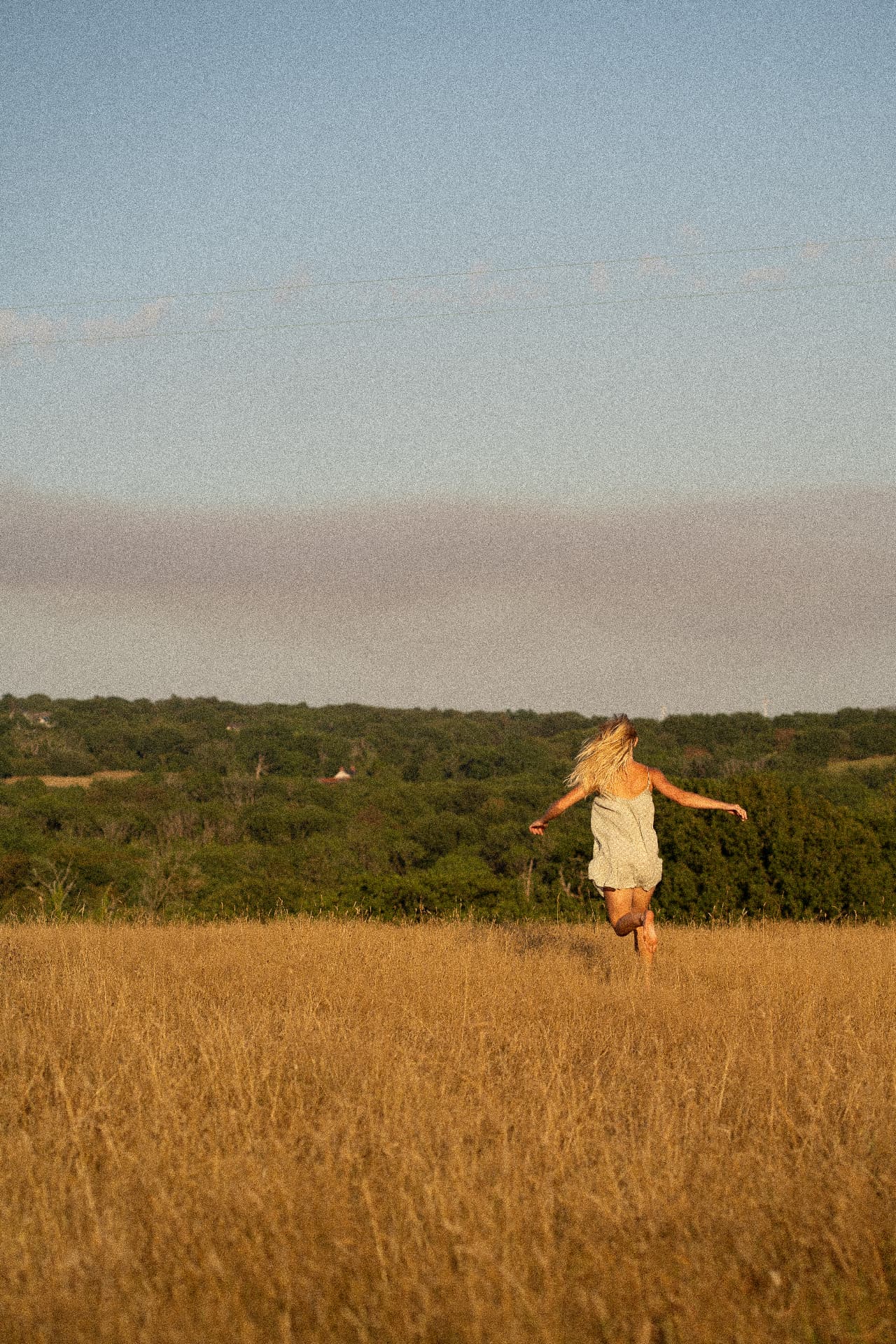 Woman running through a golden field at sunset with open arms