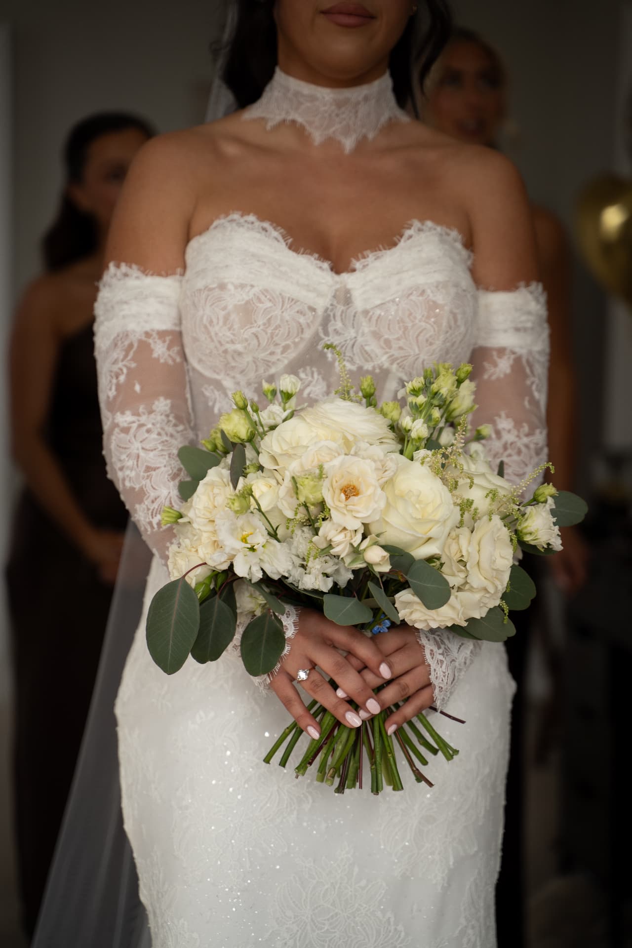 Bride in an off-the-shoulder lace wedding dress holding a white rose bouquet with eucalyptus