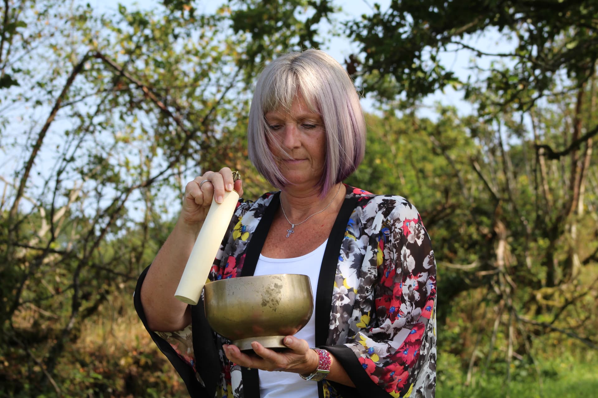 Woman holding a singing bowl outdoors among trees