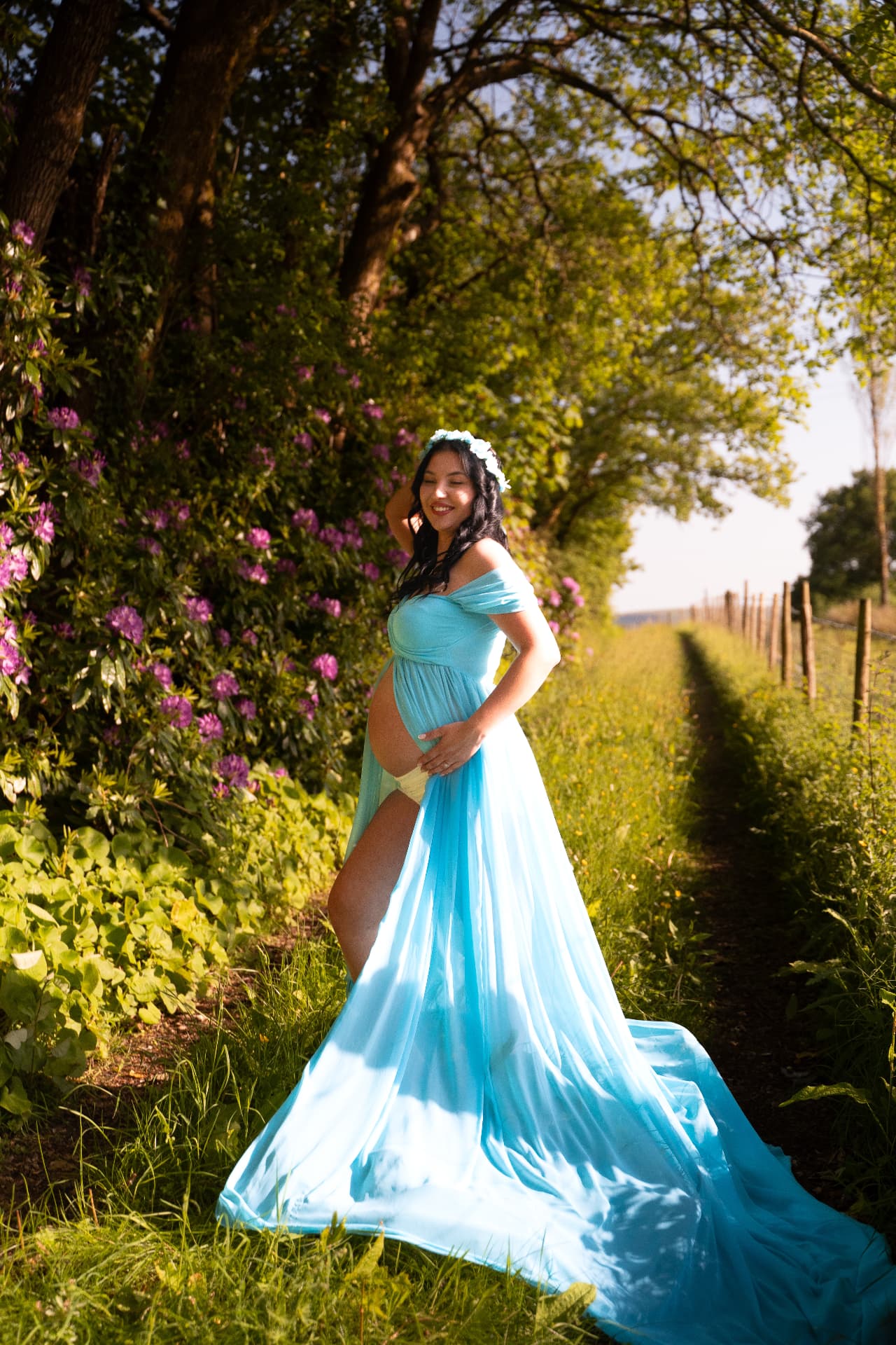 Pregnant woman in a flowing blue dress among summer garden flowers