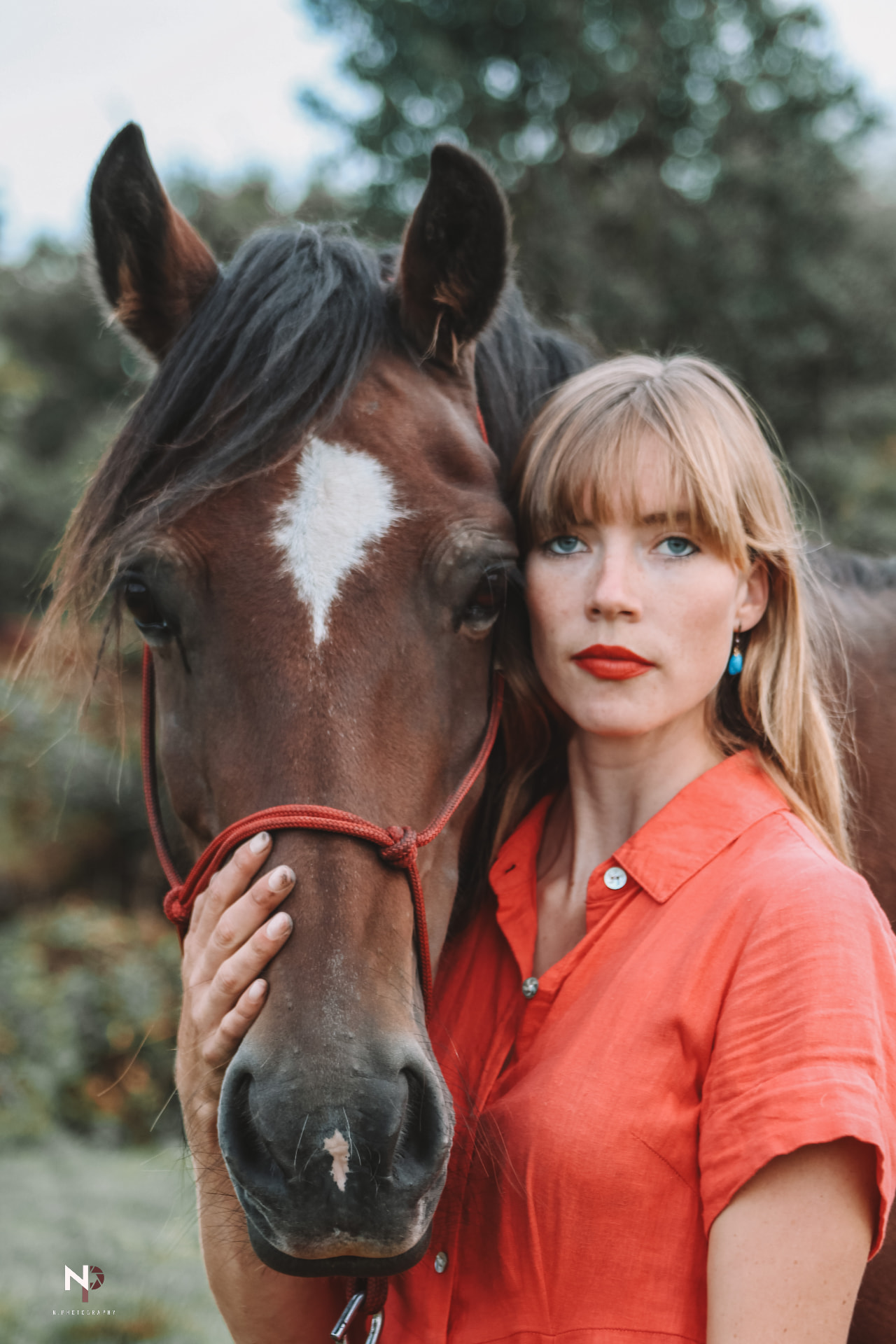 Woman in a red shirt with red lipstick standing close beside a brown horse