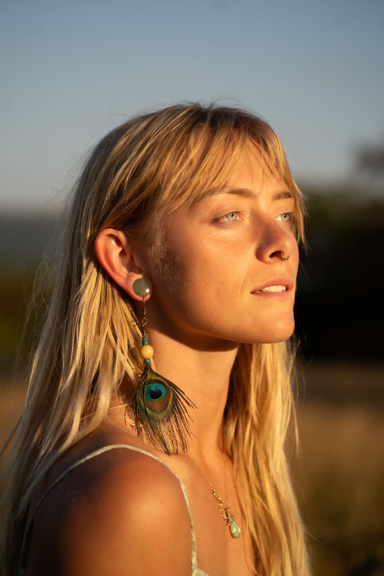 Portrait of a woman in warm golden light wearing peacock feather earrings