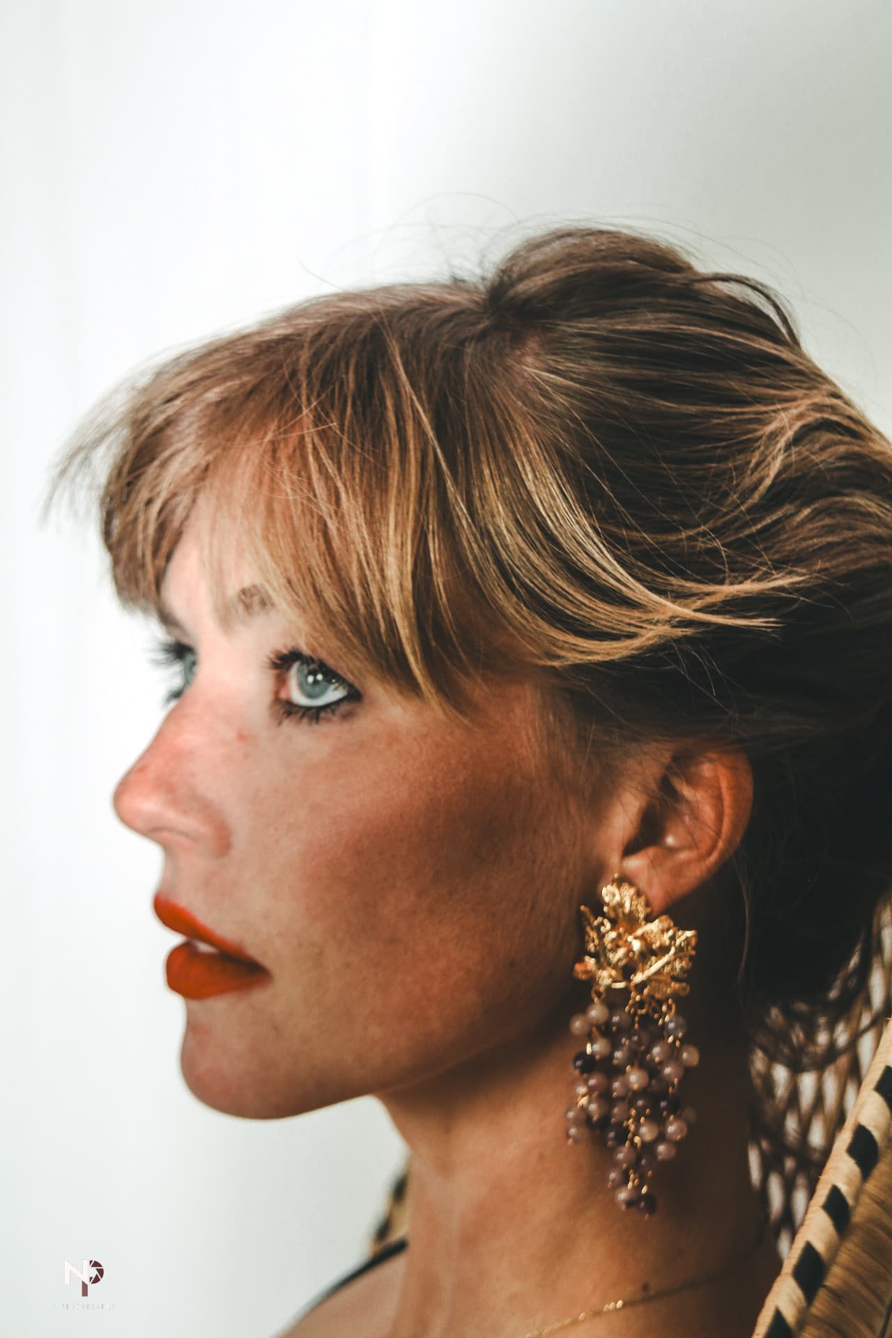 Profile portrait of a woman with tousled hair, red lipstick and a gold statement earring