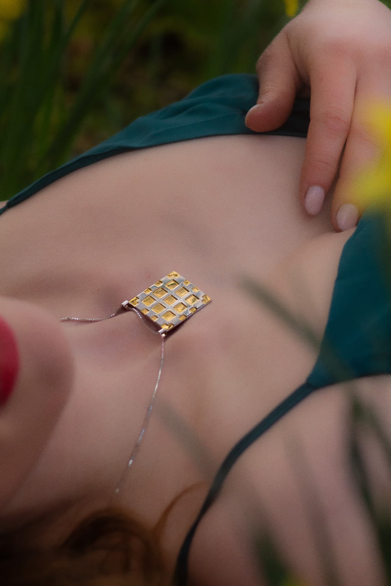 Handmade silver and gold pendant resting on skin among spring grass